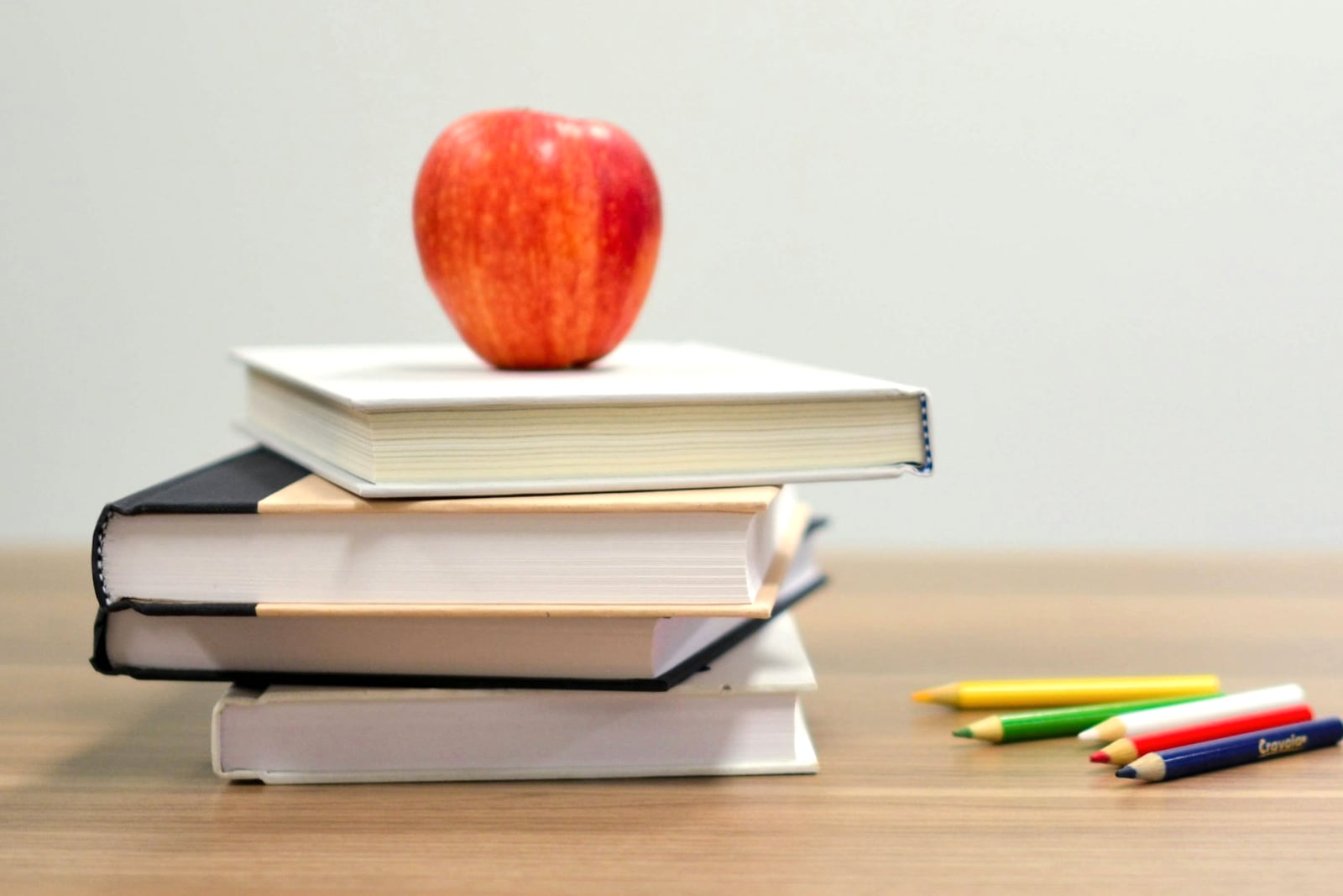 تفاحة حمراء فوق كومة من الكتب وبجانبها أقلام ملونة